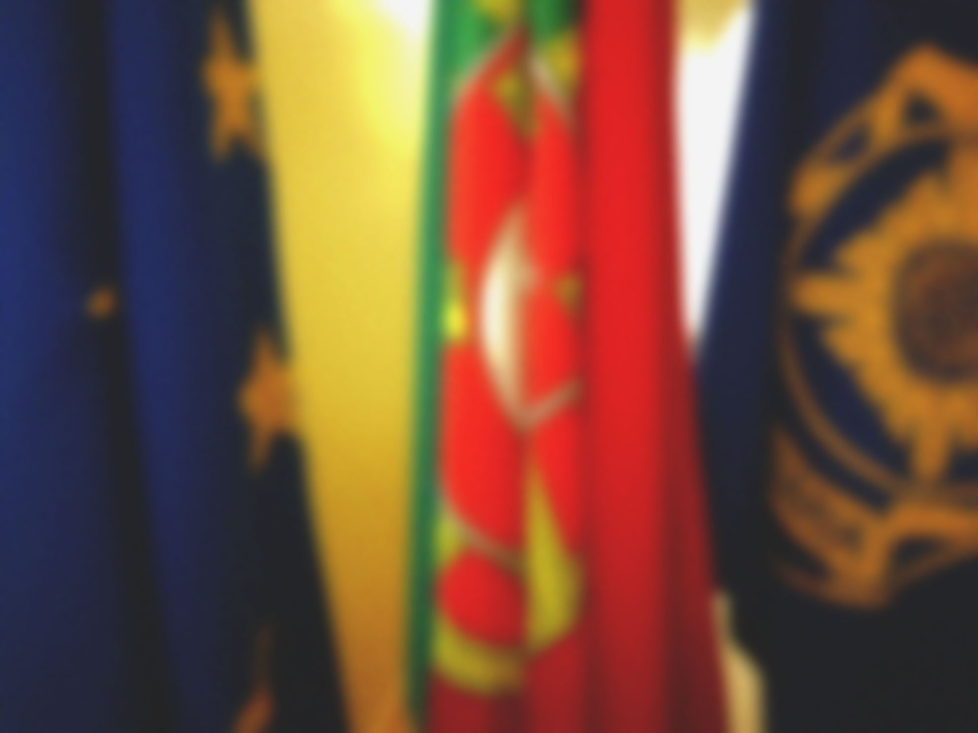 Imagem desfocada de três bandeiras: a da União Europeia, de Portugal e da Polícia Judiciária